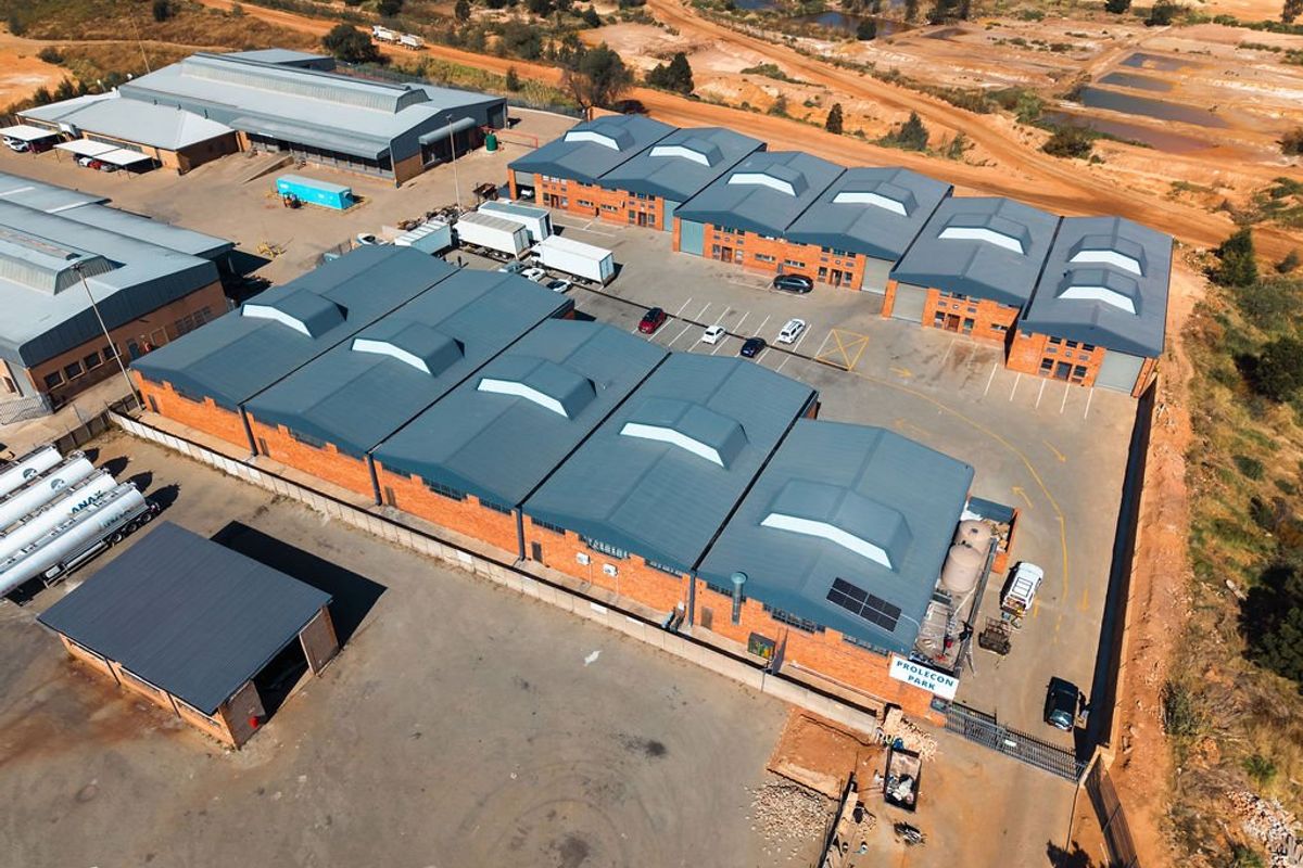 Aerial view of an industrial park featuring multiple warehouse units with metal roofing, brick facades, and a large paved yard area.