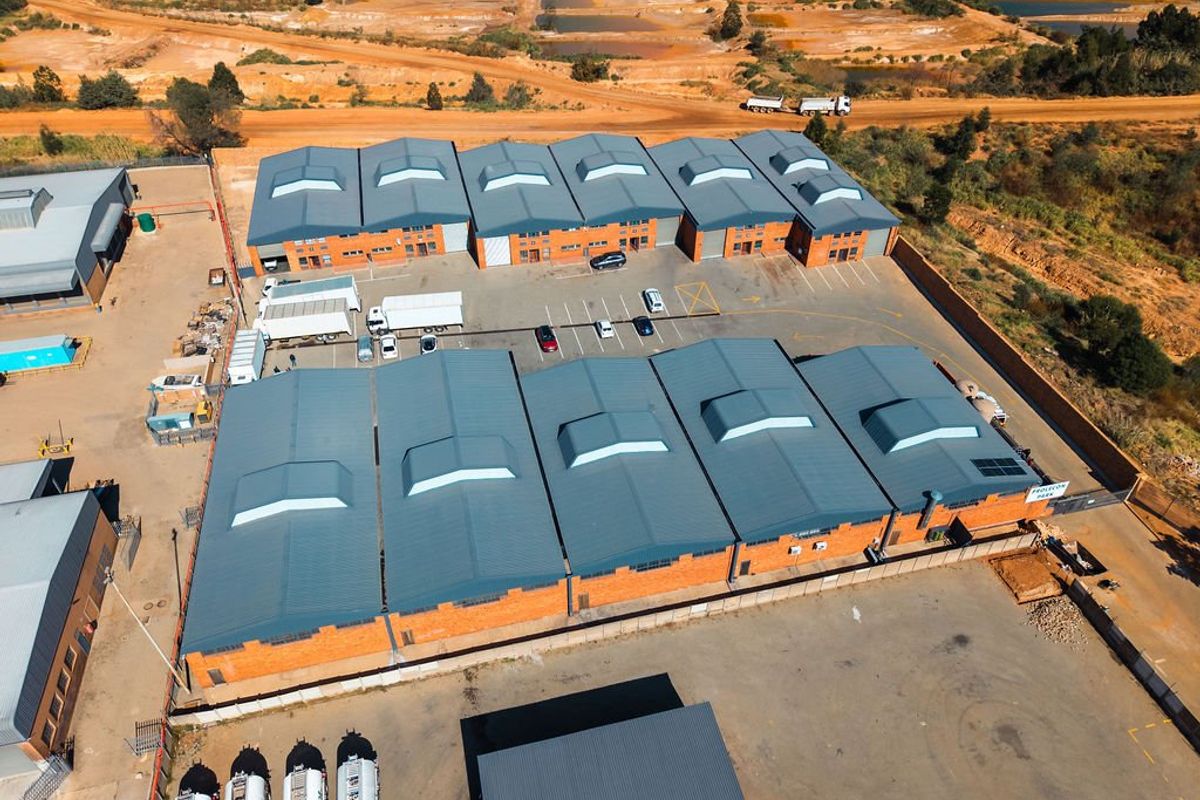 Aerial view of an industrial warehouse complex featuring multiple units with metal roofing, skylights, and a paved parking area.