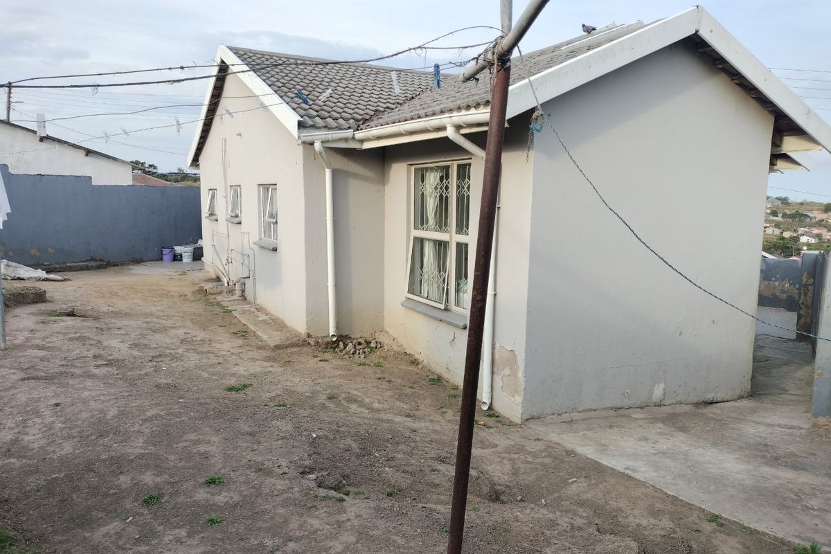 Rear view of the property showing the exterior wall, tiled roof, and surrounding yard area with basic landscaping.