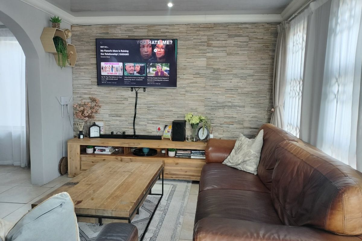 A comfortable living room featuring a textured stone veneer feature wall, recessed ceiling detail, and neutral tiled flooring.