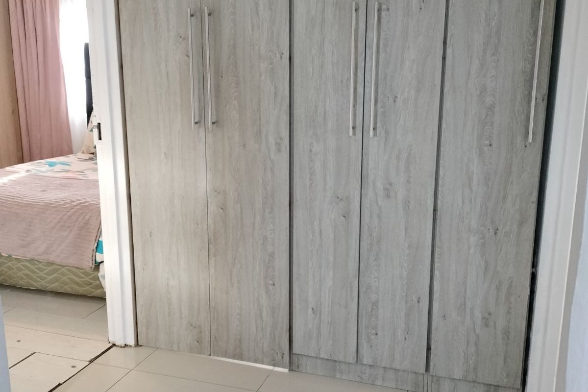 A bedroom featuring modern wood-look built-in cupboards and neutral tiled flooring, providing ample storage space.