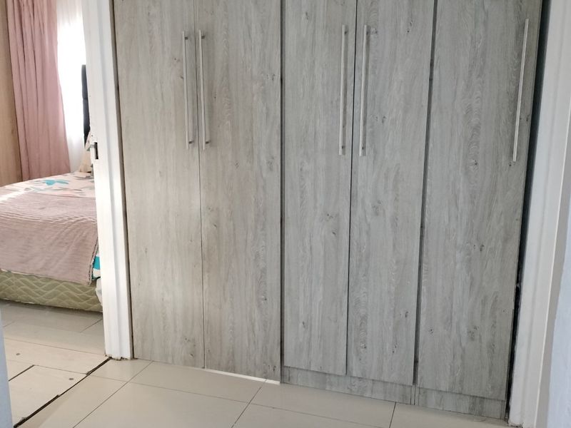 A bedroom featuring modern wood-look built-in cupboards and neutral tiled flooring, providing ample storage space.