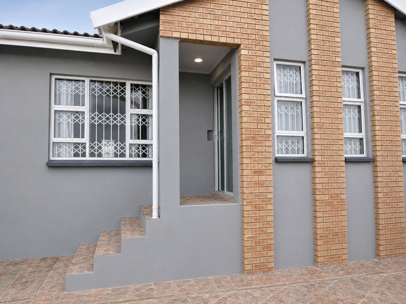 A well-maintained front entrance featuring a modern grey facade with brick accents, tiled steps, and secure window bars.