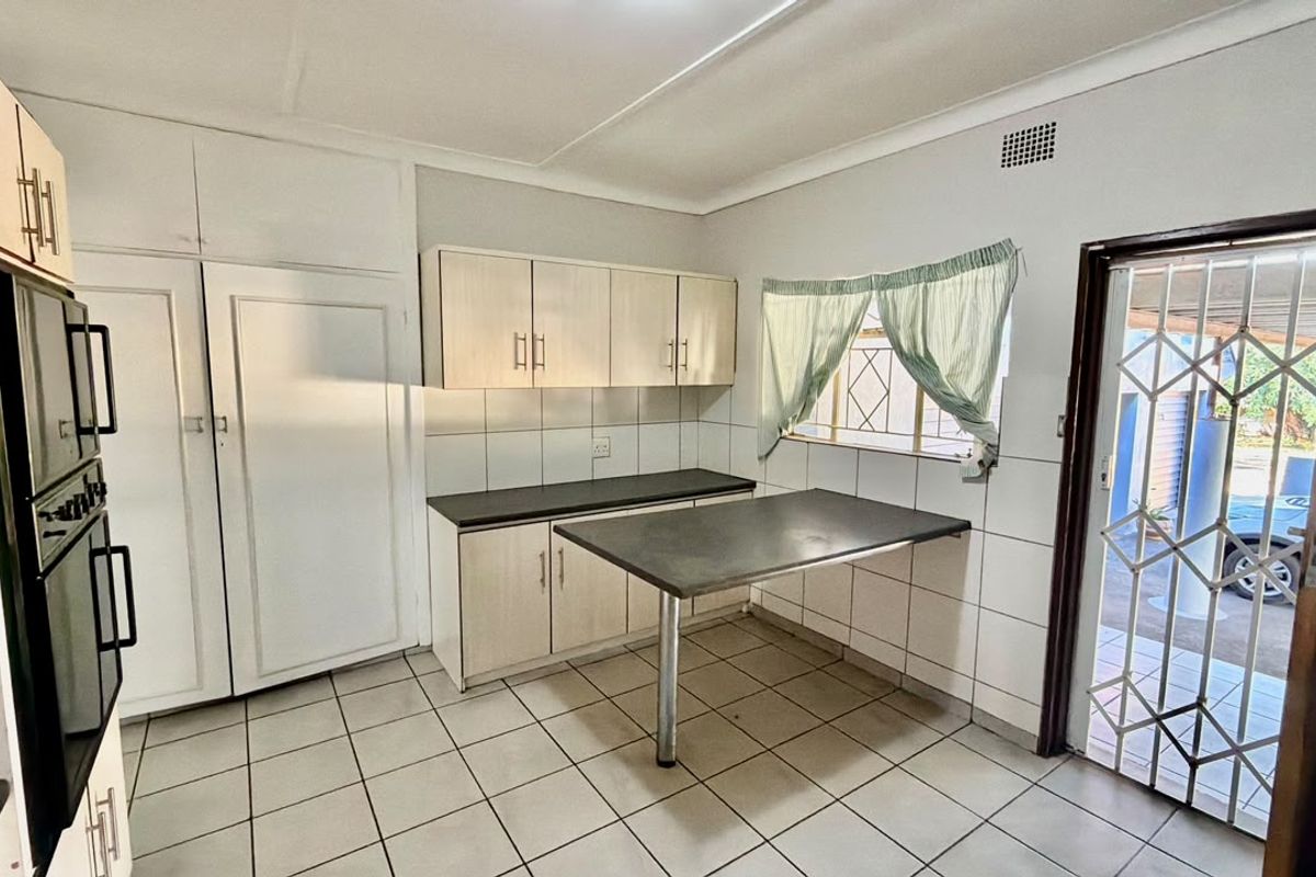 A functional kitchen featuring built-in cabinetry, a breakfast counter, tiled flooring, and direct access to the exterior via a security gate.
