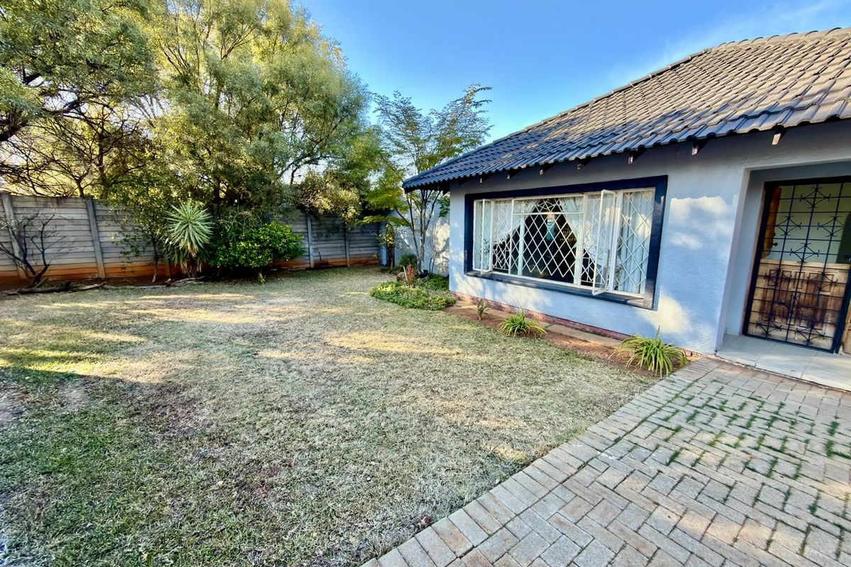 Rear exterior view of the property featuring a paved walkway, lawn area, and secure window and door fixtures.