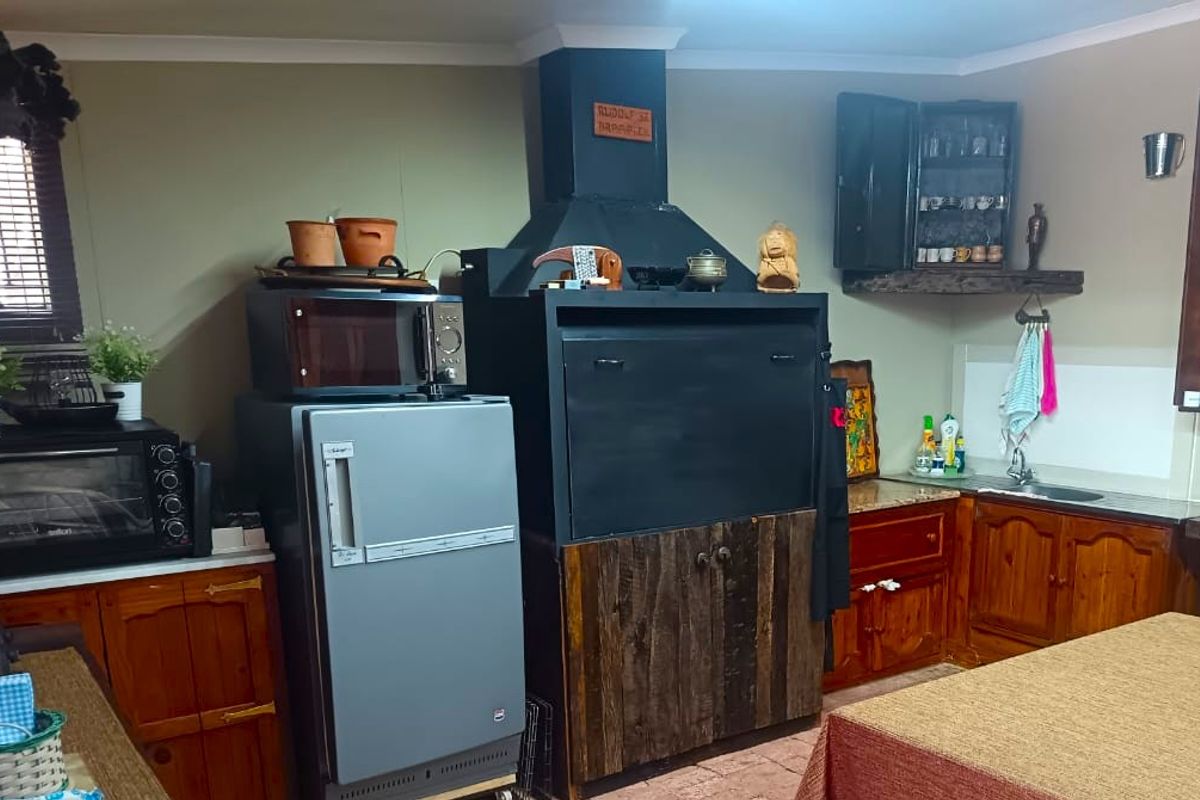 A rustic kitchen featuring wooden cabinetry, a built-in indoor braai, and tiled flooring, offering a traditional and functional cooking and entertainment space.