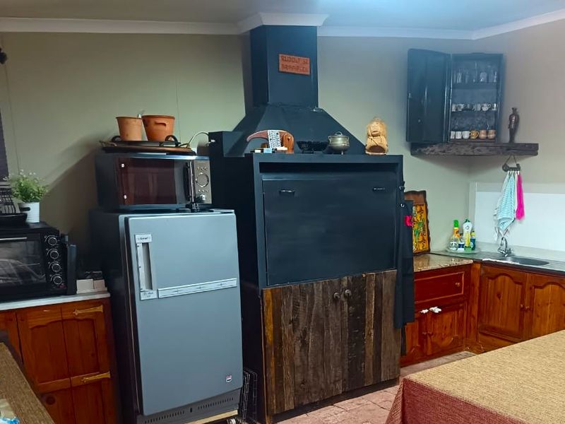 A rustic kitchen featuring wooden cabinetry, a built-in indoor braai, and tiled flooring, offering a traditional and functional cooking and entertainment space.