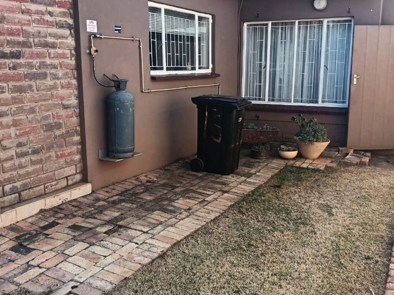 Rear exterior view of the house featuring brick paving, a tiled roof, security bars on windows, and an external gas cylinder installation.