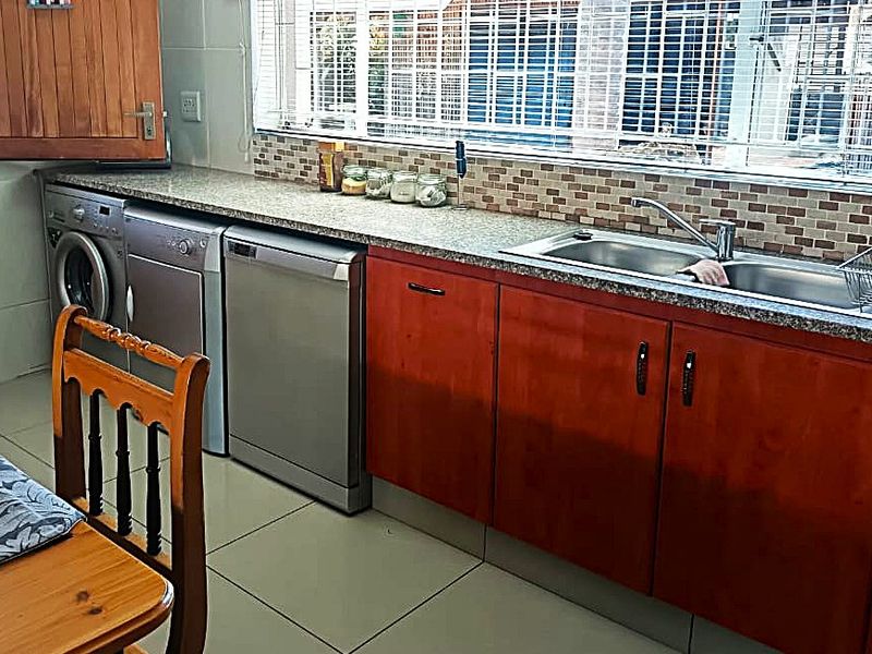 A functional kitchen featuring wooden cabinetry, granite countertops, a double stainless steel sink, and tiled flooring with a tiled backsplash.