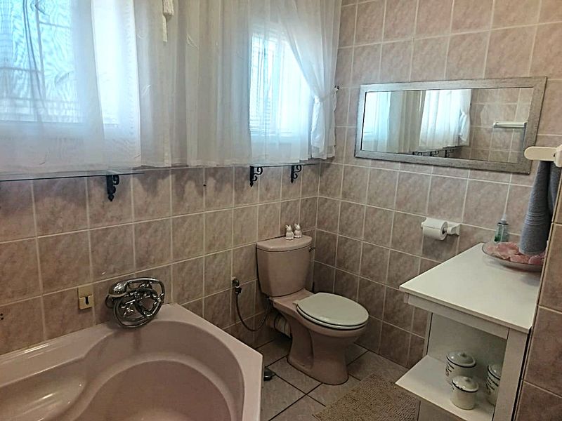 A functional bathroom featuring a corner bathtub, toilet, and vanity cabinet with full-height wall tiling and tiled flooring.