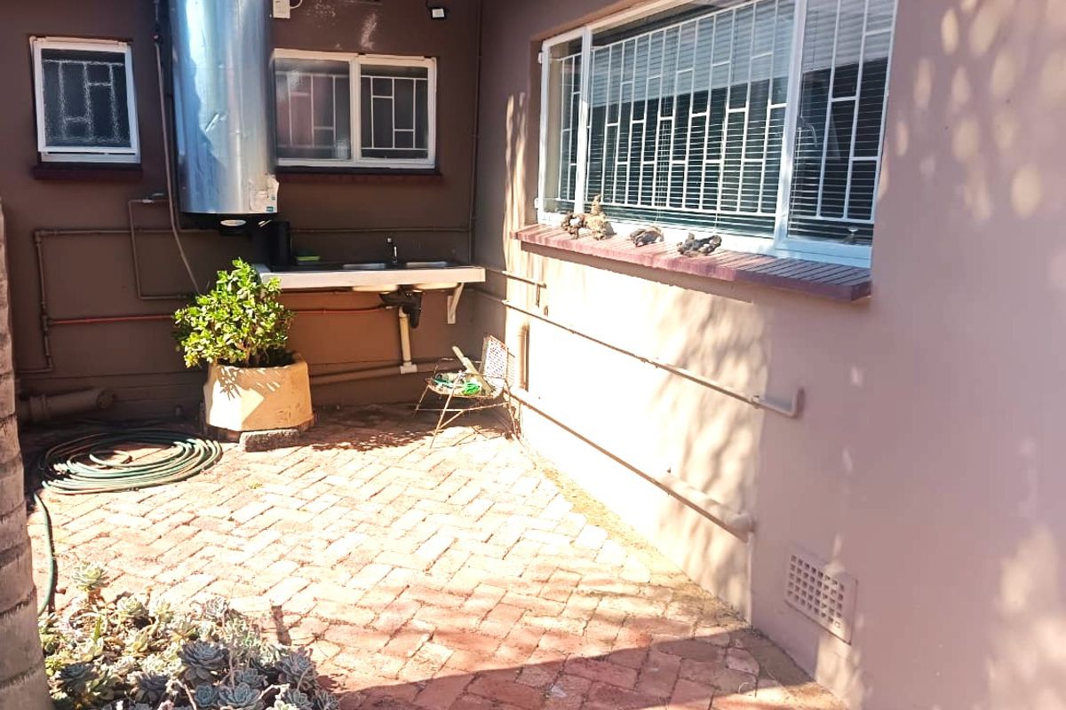 Rear exterior area featuring brick paving, an external sink, and a wall-mounted geyser with security bars on the windows.