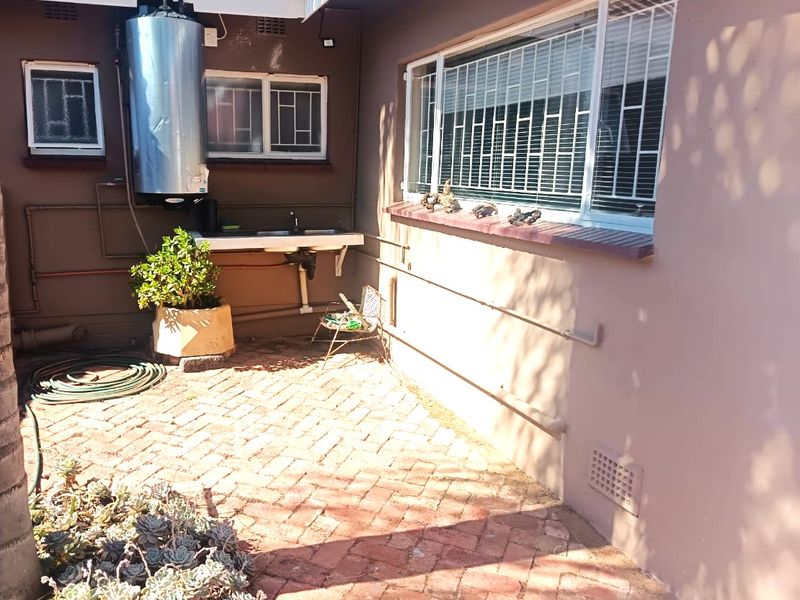 Rear exterior area featuring brick paving, an external sink, and a wall-mounted geyser with security bars on the windows.