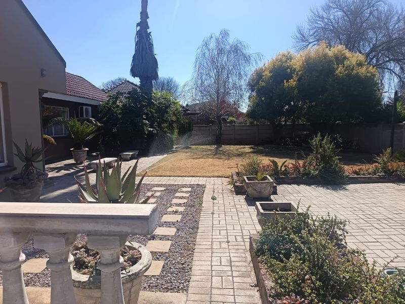 A spacious rear garden featuring a paved patio area, concrete balustrade, established landscaping, and a functional sprinkler system.