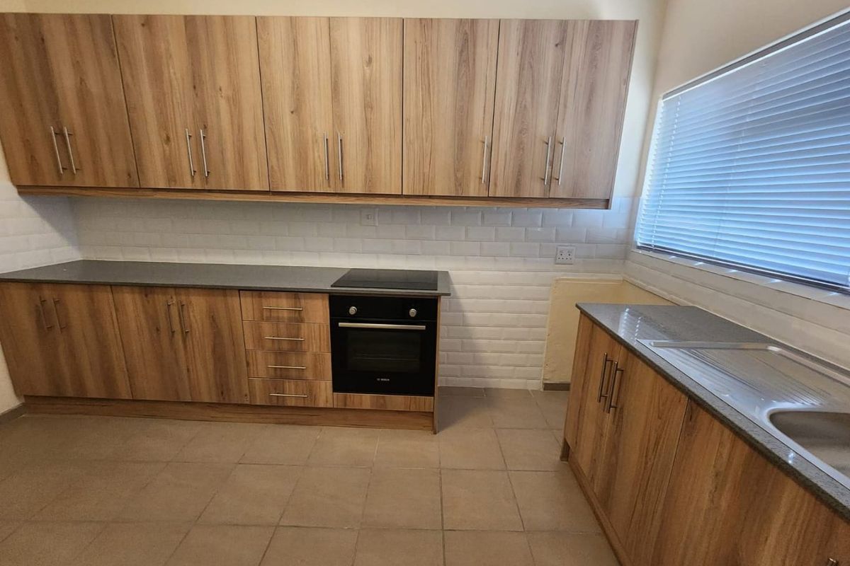 A functional kitchen featuring wood-look cabinetry, dark countertops, a built-in oven and hob, and a classic white subway tile backsplash.