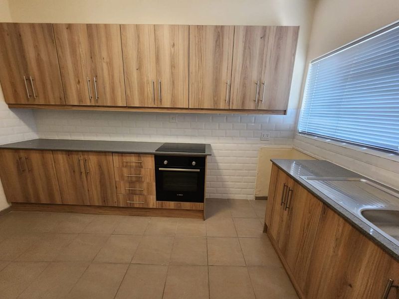 A functional kitchen featuring wood-look cabinetry, dark countertops, a built-in oven and hob, and a classic white subway tile backsplash.