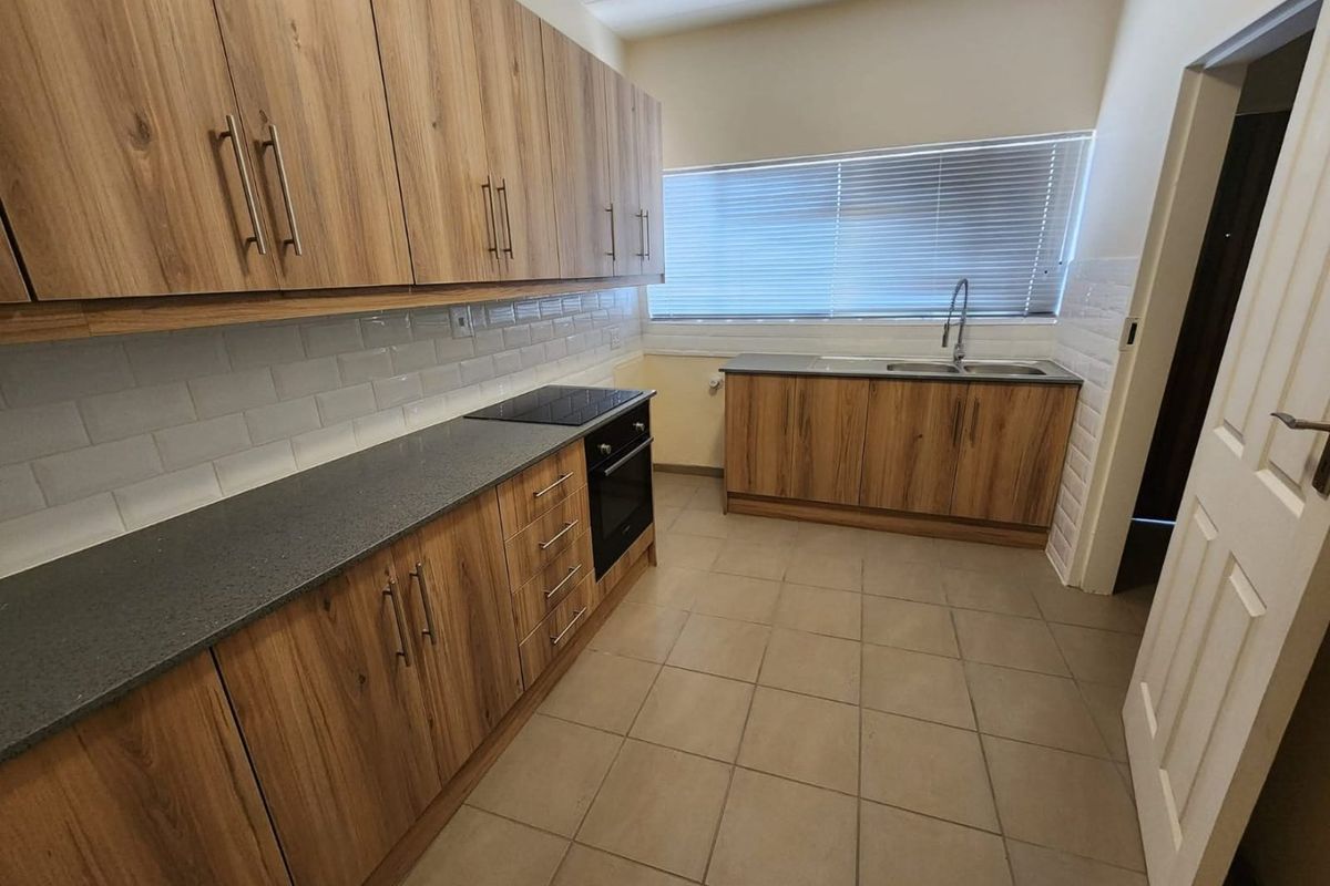 Modern kitchen featuring wood-look cabinetry, dark countertops, built-in oven and hob, subway tile backsplash, and ceramic floor tiles.