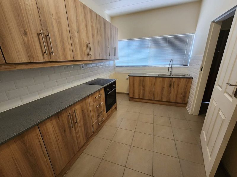 Modern kitchen featuring wood-look cabinetry, dark countertops, built-in oven and hob, subway tile backsplash, and ceramic floor tiles.