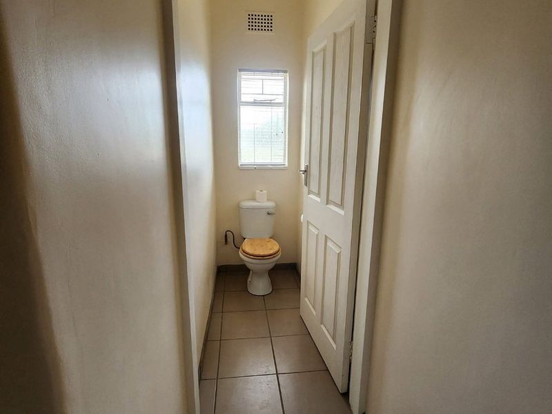 A compact, functional guest toilet featuring tiled flooring, a window for natural light, and a ventilation grille.