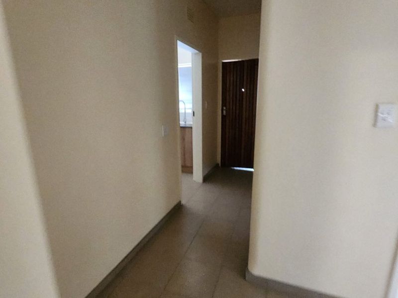 A simple, tiled hallway providing access to other areas of the apartment, featuring neutral walls and a wooden door.