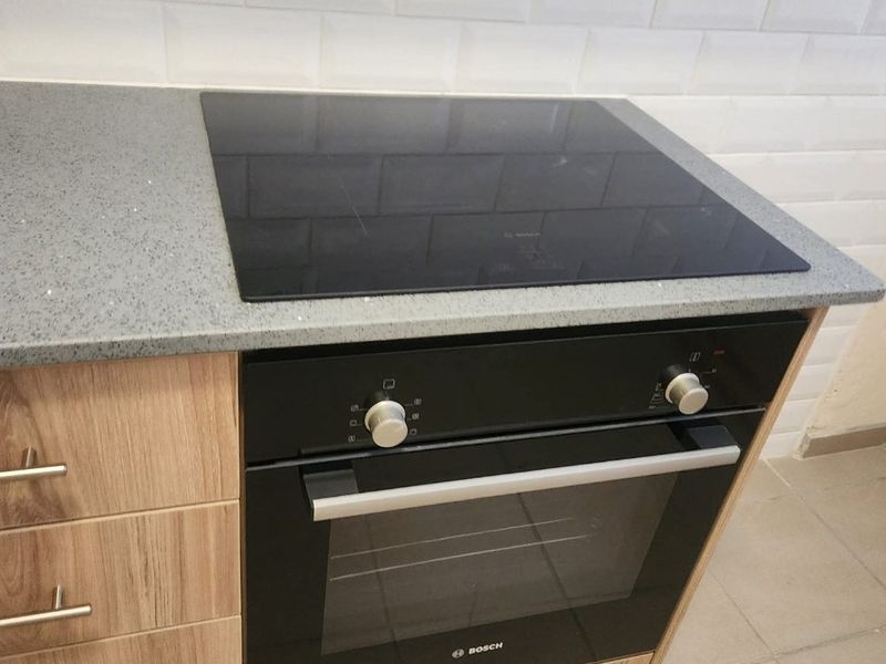 Modern kitchen featuring a built-in Bosch oven, induction hob, stone countertop, and classic white subway tile backsplash with wood-finish cabinetry.