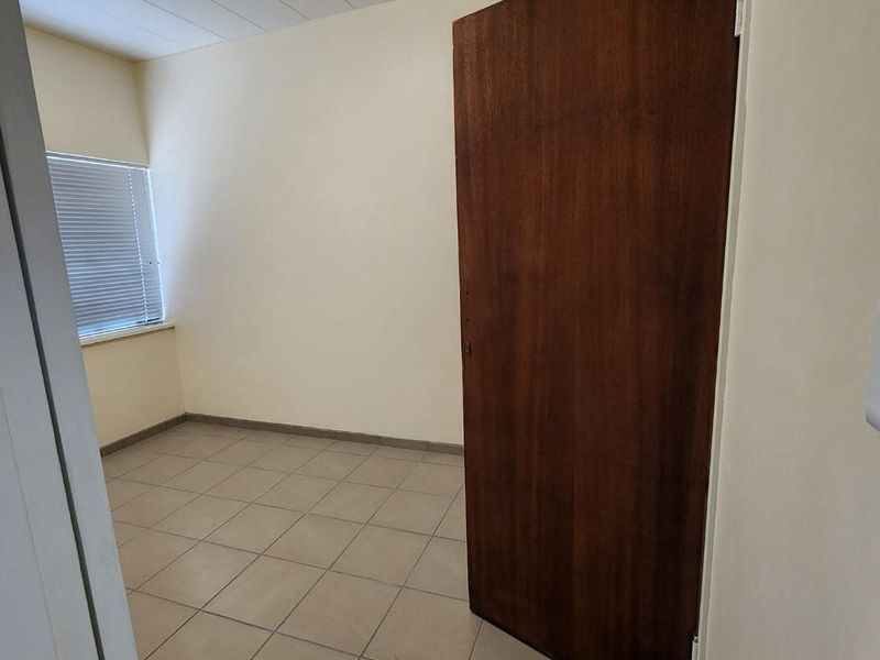 A clean, empty bedroom featuring neutral tiled flooring, a wooden door, and a window fitted with venetian blinds.