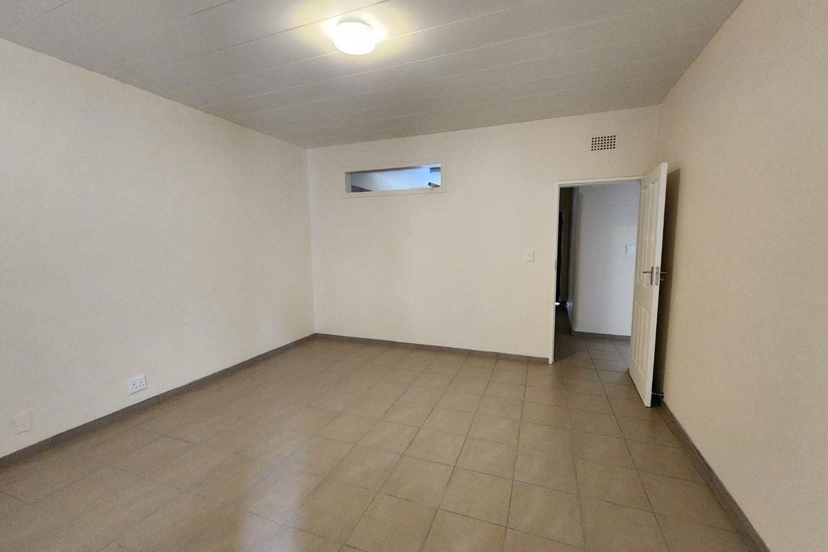 A clean, empty bedroom featuring neutral tiled flooring, a high-level window, and a standard internal door, providing a blank canvas for personalization.