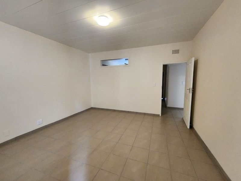 A clean, empty bedroom featuring neutral tiled flooring, a high-level window, and a standard internal door, providing a blank canvas for personalization.