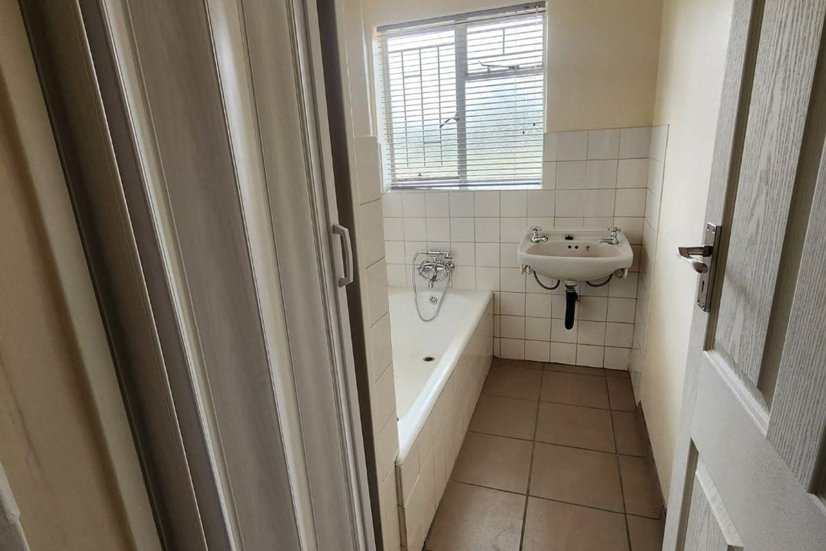 A functional bathroom featuring a bathtub, wall-mounted basin, tiled splashback, and tiled flooring, accessible via a folding door.