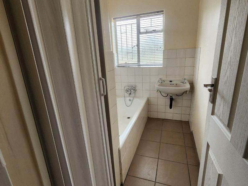 A functional bathroom featuring a bathtub, wall-mounted basin, tiled splashback, and tiled flooring, accessible via a folding door.