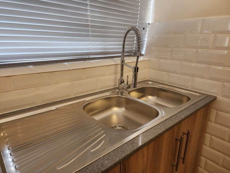 A clean kitchen area featuring a stainless steel double sink with a modern gooseneck faucet, subway tile backsplash, and wood-finish cabinetry.