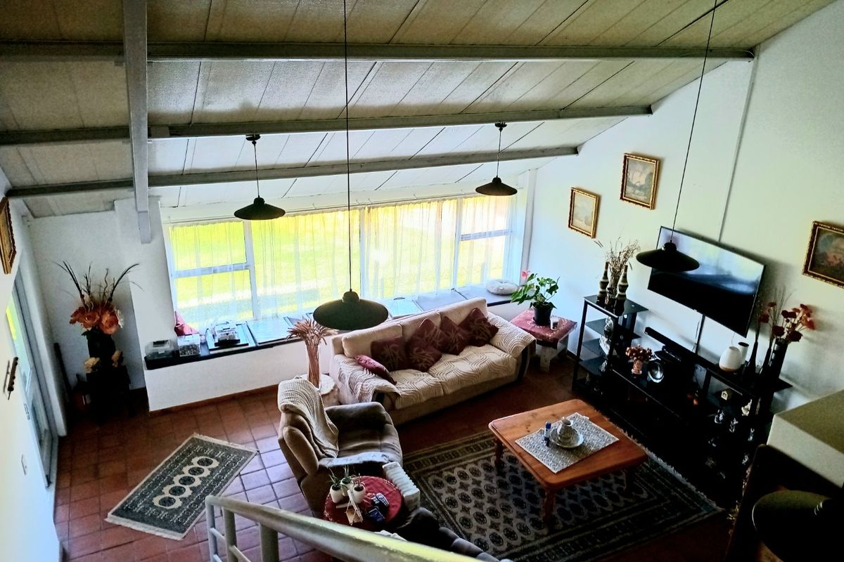 Spacious living area featuring a high vaulted ceiling with exposed rafters, large windows providing ample natural light, and durable tiled flooring.