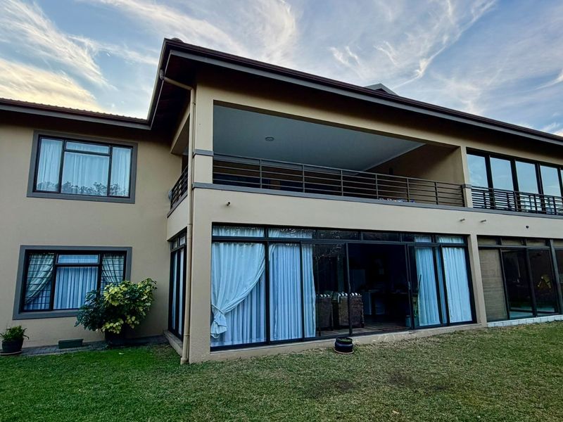 Rear view of a two-story residential property featuring a spacious covered balcony, large sliding glass doors, and a well-maintained lawn.