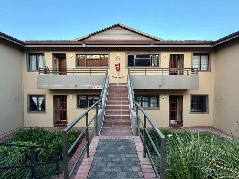 Exterior view of a two-story apartment complex featuring a central tiled staircase, metal handrails, and private balconies for the upper units.