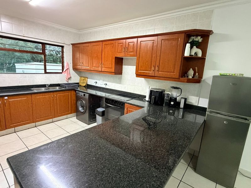 A functional kitchen featuring wooden cabinetry, granite countertops, a tiled backsplash, and a breakfast bar area with integrated appliances.