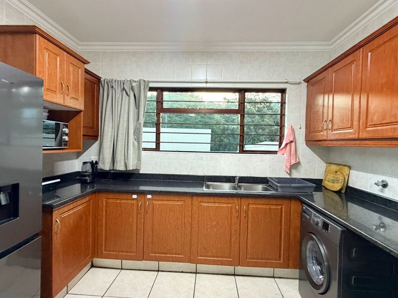 A functional kitchen featuring wooden cabinetry, granite countertops, a double basin sink, and tiled finishes, offering a practical layout for daily use.