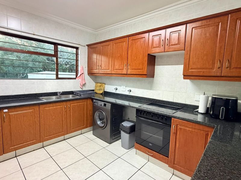 A functional kitchen featuring wooden cabinetry, granite countertops, a built-in oven with hob, and tiled flooring with a double basin sink.