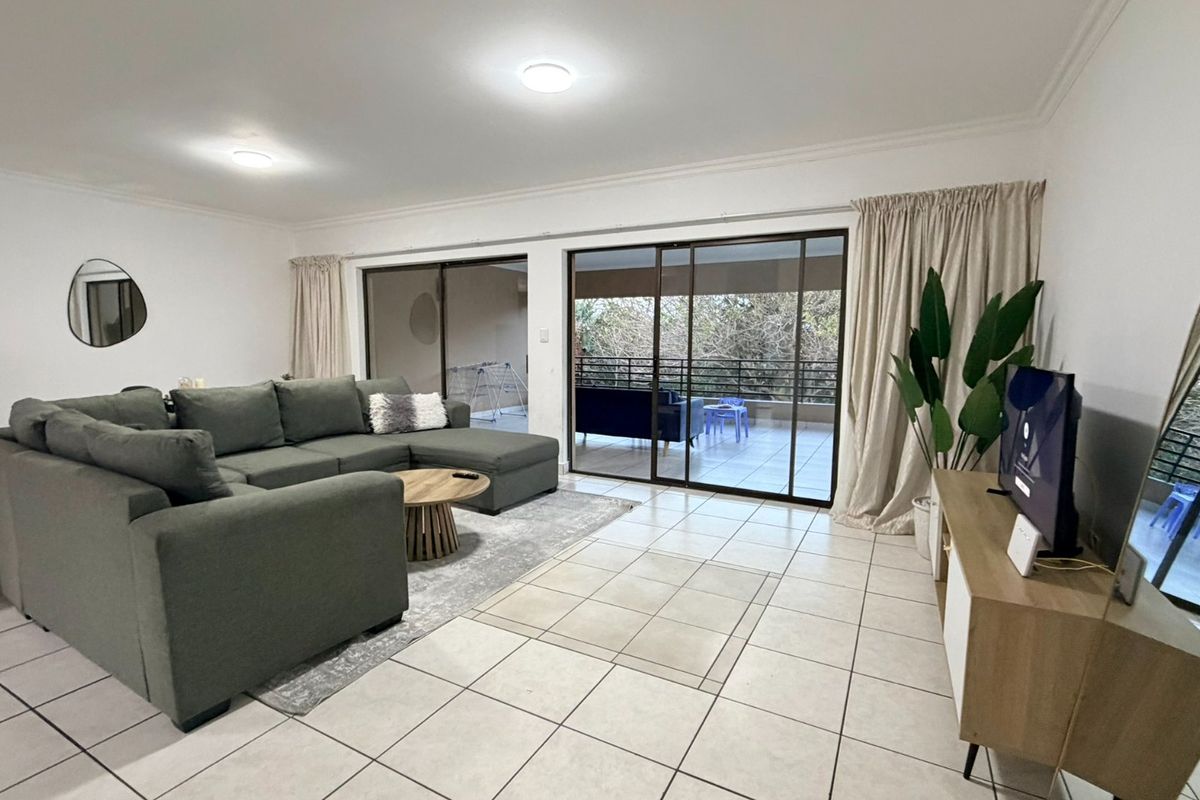 Spacious living room featuring large sliding glass doors that open onto a balcony, providing ample natural light and tiled flooring throughout.