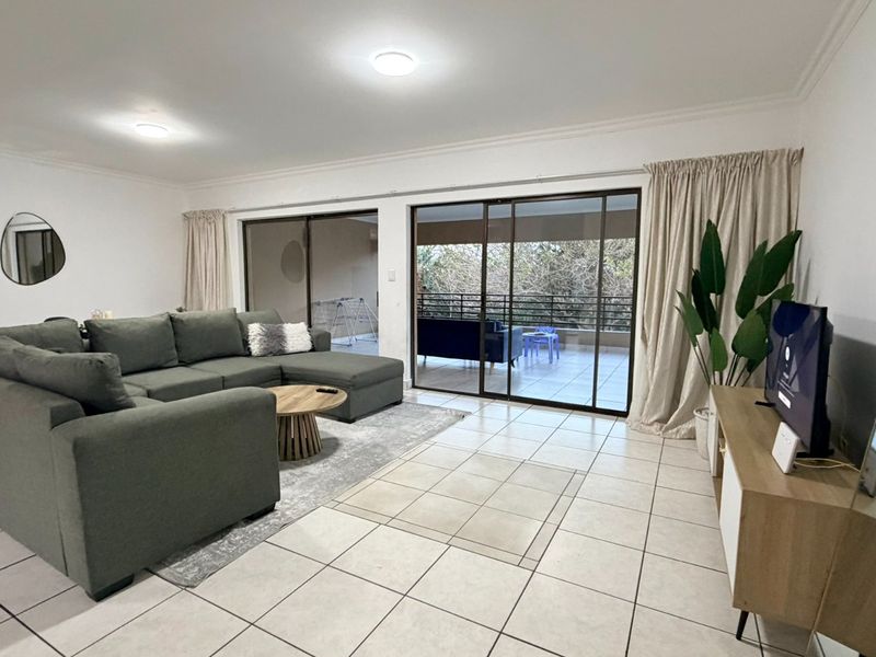 Spacious living room featuring large sliding glass doors that open onto a balcony, providing ample natural light and tiled flooring throughout.