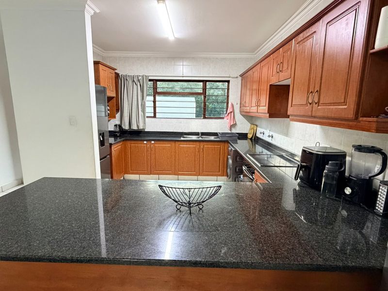 A functional kitchen featuring wooden cabinetry, granite countertops, a double sink, and tiled backsplash, offering a classic layout with ample storage space.