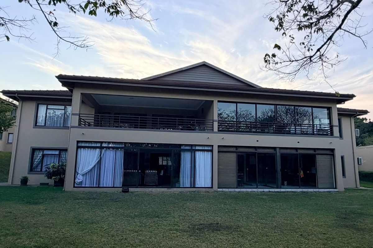Rear view of a multi-story apartment building featuring a spacious balcony, large sliding glass doors, and expansive windows overlooking a landscaped lawn.