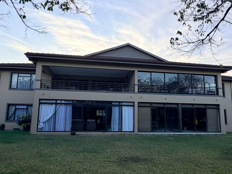 Rear view of a multi-story apartment building featuring a spacious balcony, large sliding glass doors, and expansive windows overlooking a landscaped lawn.