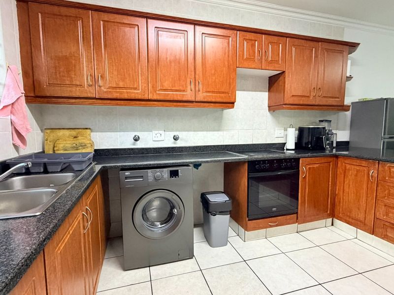 A functional kitchen featuring warm-toned wooden cabinetry, granite countertops, a built-in oven, and tiled flooring with a practical layout.