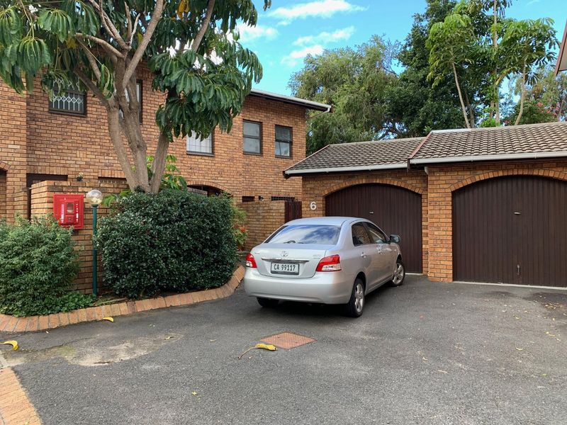Front exterior view of a face brick townhouse featuring a double garage, asphalt driveway, and established garden area.
