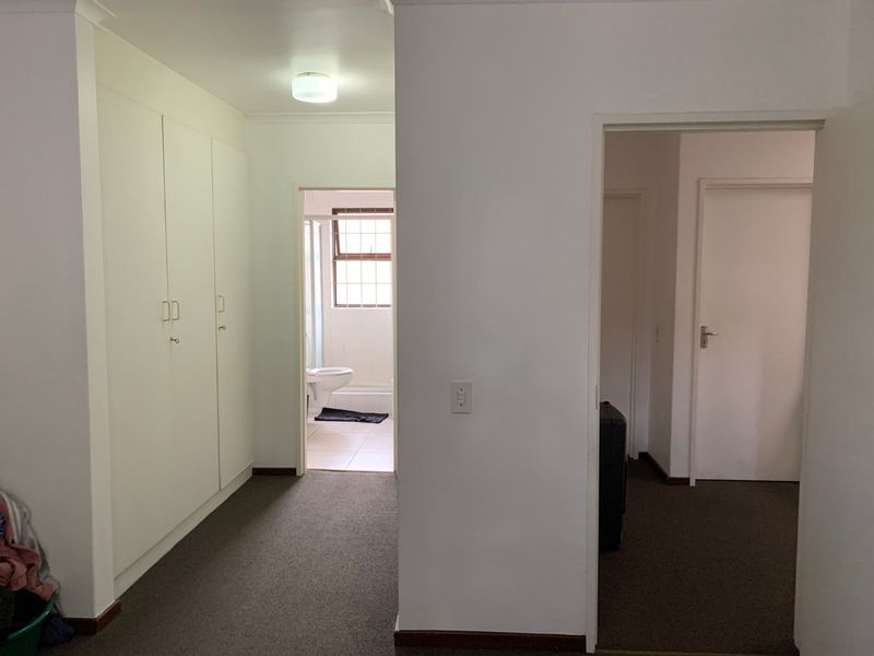 A functional hallway featuring built-in cupboards, carpeted flooring, and direct access to an adjoining bathroom and other rooms.