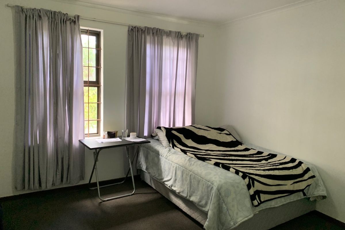 A standard bedroom featuring carpeted flooring, neutral walls, and windows fitted with security bars and curtain rails.