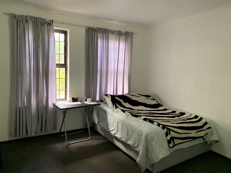 A standard bedroom featuring carpeted flooring, neutral walls, and windows fitted with security bars and curtain rails.