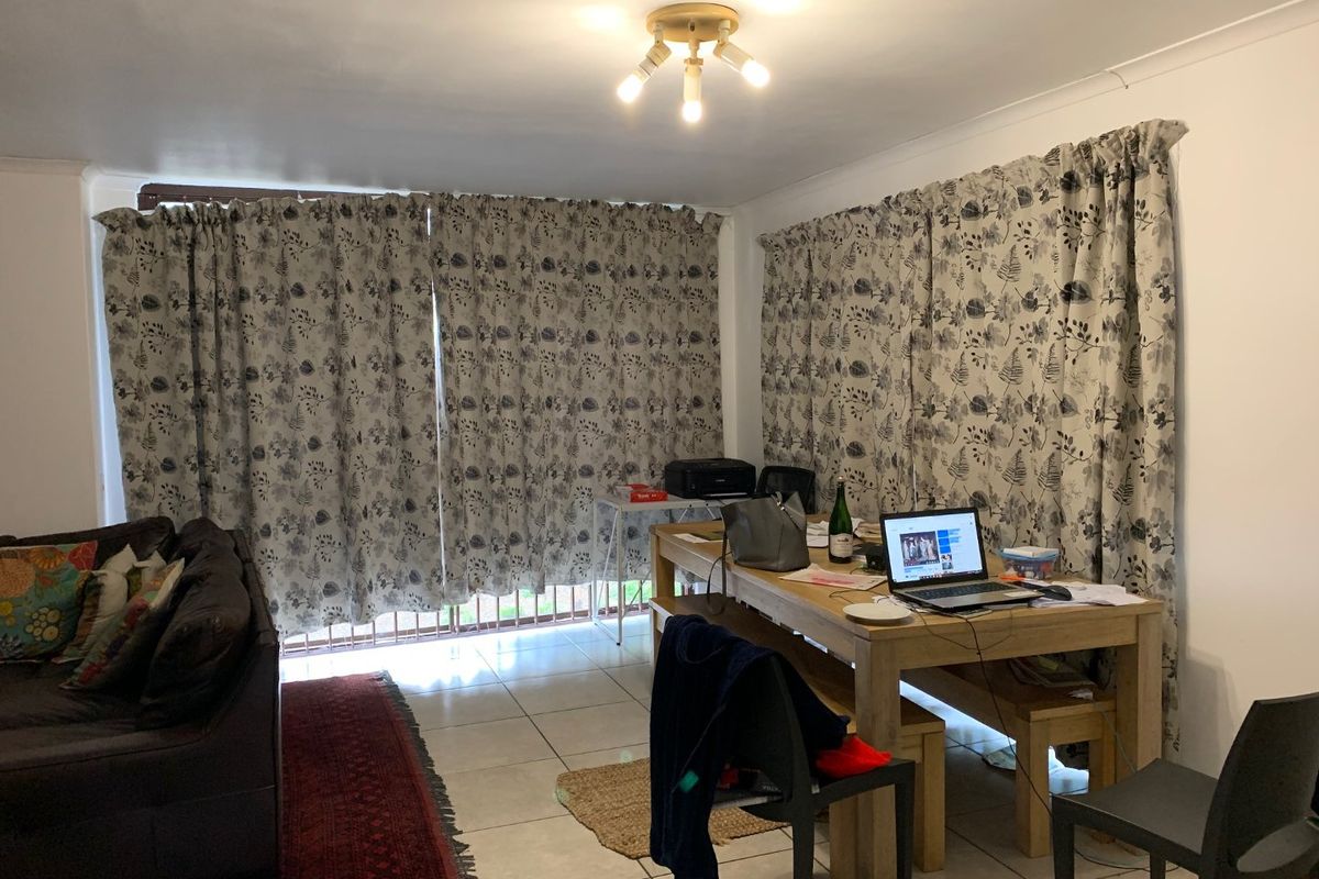A living area featuring tiled flooring and large windows covered by curtains, providing a functional space for relaxation or dining.