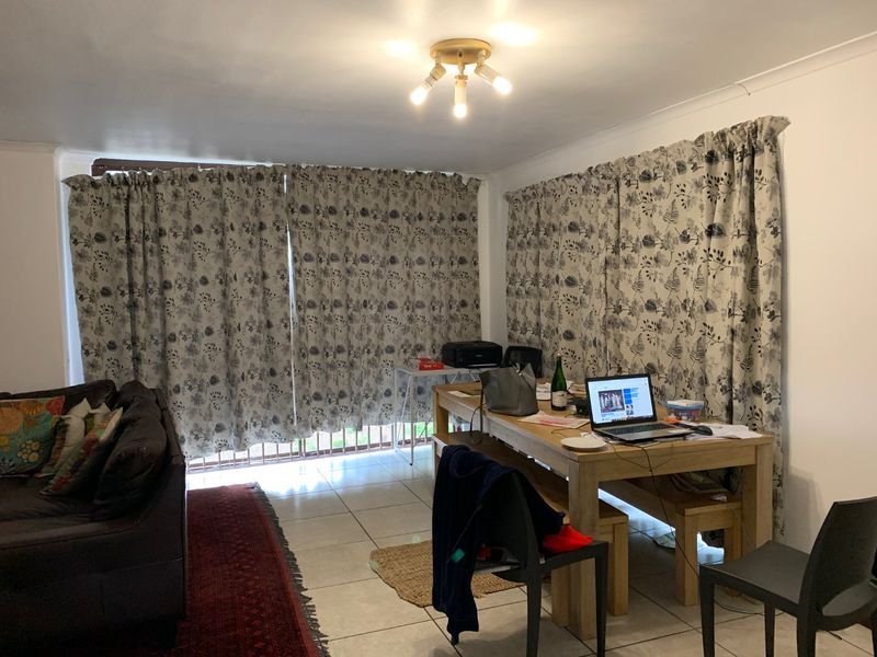 A living area featuring tiled flooring and large windows covered by curtains, providing a functional space for relaxation or dining.