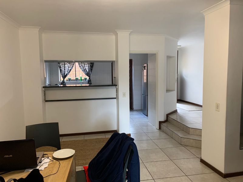 Open plan living area featuring tiled flooring, a breakfast bar serving the kitchen, and a small internal staircase leading to an adjacent hallway.