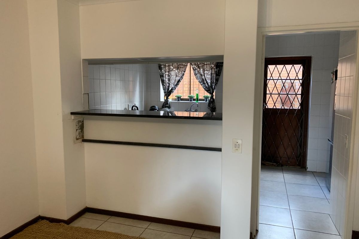 A functional kitchen area featuring a breakfast bar, tiled flooring, and a direct view into the adjacent utility space with a secure rear door.